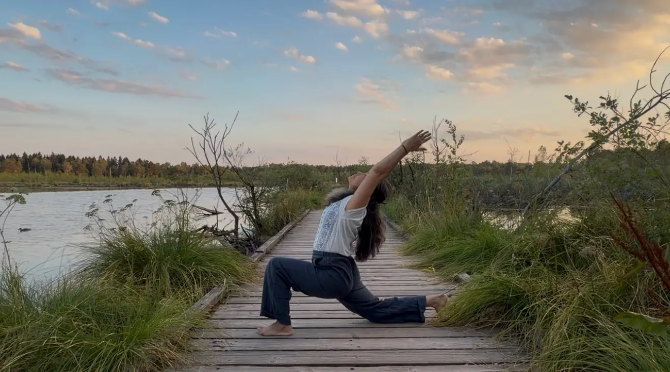 Yoga-Haltung mit Rückbeuge im Ausfallschritt auf einem Holzsteg am See im Abendlicht